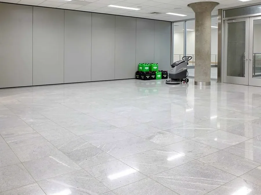 Polished stone floor in a commercial lobby with a floor scrubber and cleaning products ready for use